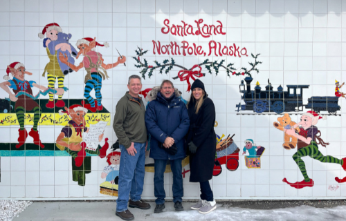 Marty, Becca and Brian in the town of North Pole posing for a group photo in front of a Christmas mural